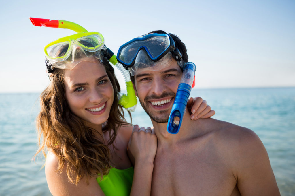 Portrait of smiling young couple wearing scuba masks at beach on sunny day